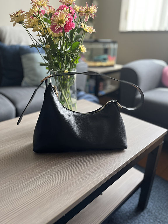 black handbag on a coffee table with flowers in the back